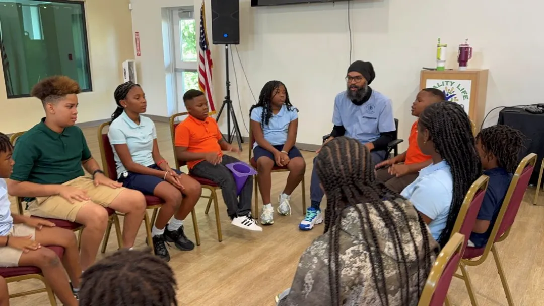 A diverse group of kids in casual attire sits in a circle, engaged in conversation during a group activity in a community space.